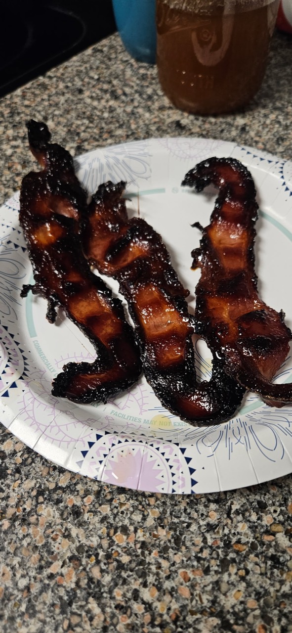 Finished dark, crispy candied bacon on a plate
