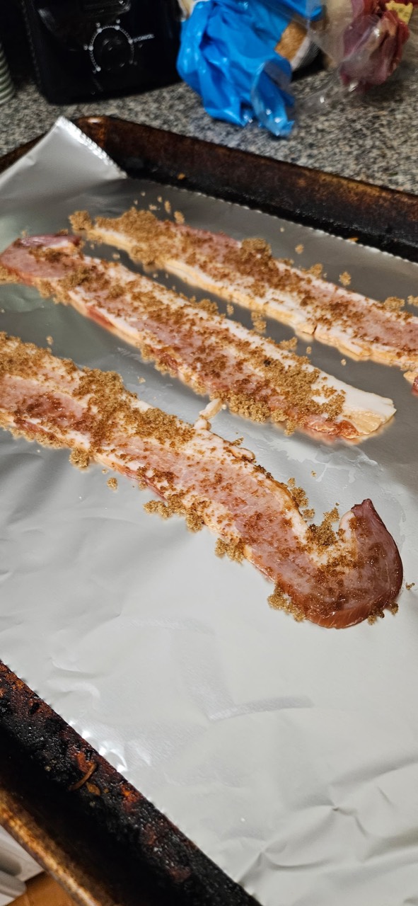 Raw bacon coated with brown sugar on a foil-lined baking sheet