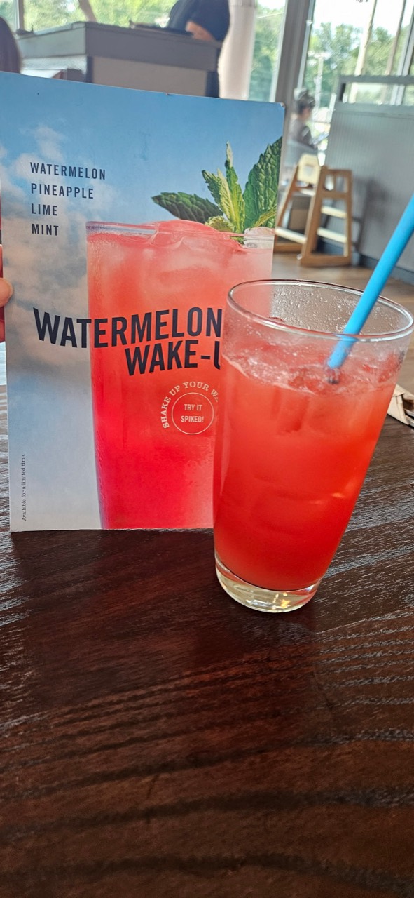 A red Watermelon Wake-Up drink beside a menu listing watermelon, pineapple, lime, and mint
